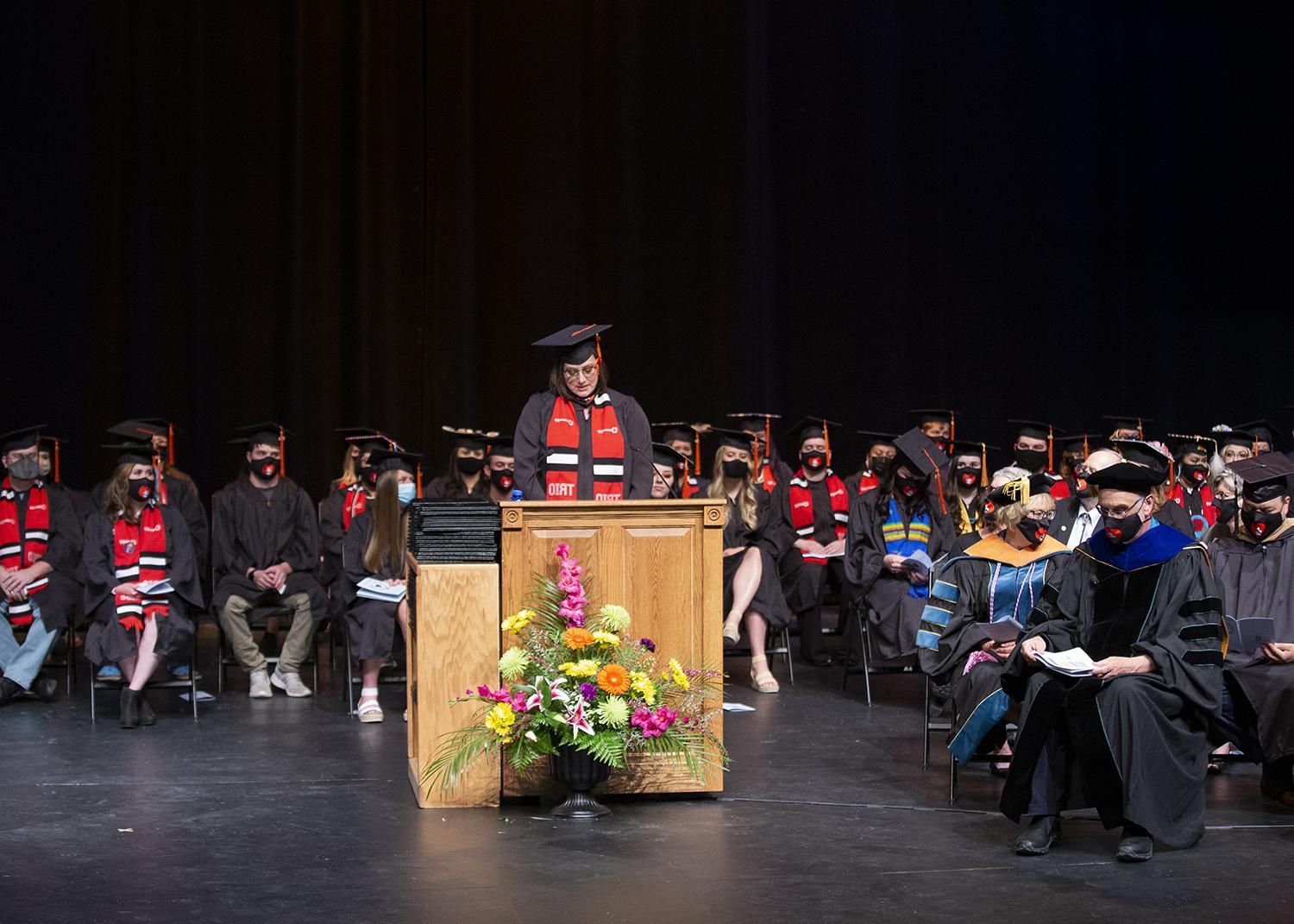 graduate speaker stands at the podium with graduates on stage